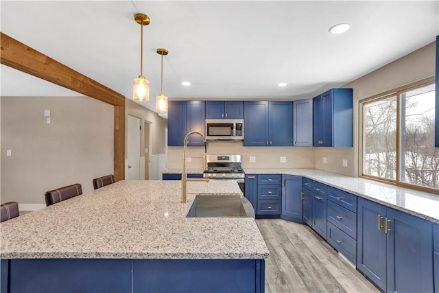 kitchen featuring stainless steel appliances, a kitchen island with sink, a kitchen breakfast bar, blue cabinets, and hanging light fixtures