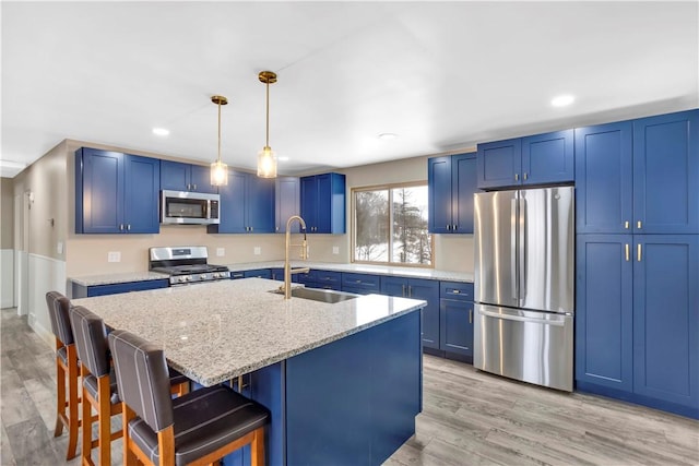 kitchen with sink, a kitchen island with sink, appliances with stainless steel finishes, a kitchen breakfast bar, and light stone counters