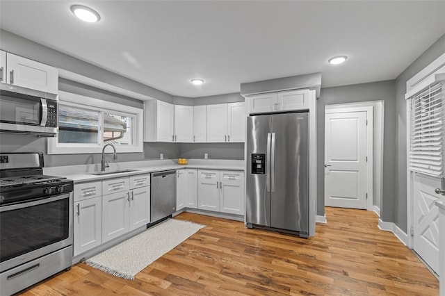 kitchen featuring light wood-type flooring, appliances with stainless steel finishes, white cabinetry, and sink