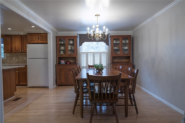 dining area with light hardwood / wood-style floors, an inviting chandelier, and crown molding