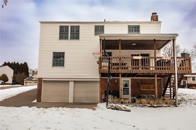 snow covered rear of property with a garage and a wooden deck