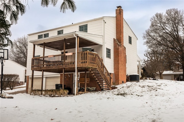 snow covered rear of property with a garage and a wooden deck