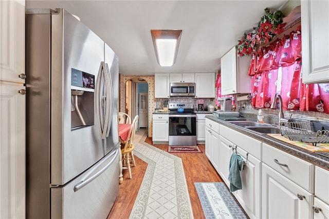 kitchen featuring sink, white cabinetry, light wood-type flooring, decorative backsplash, and appliances with stainless steel finishes