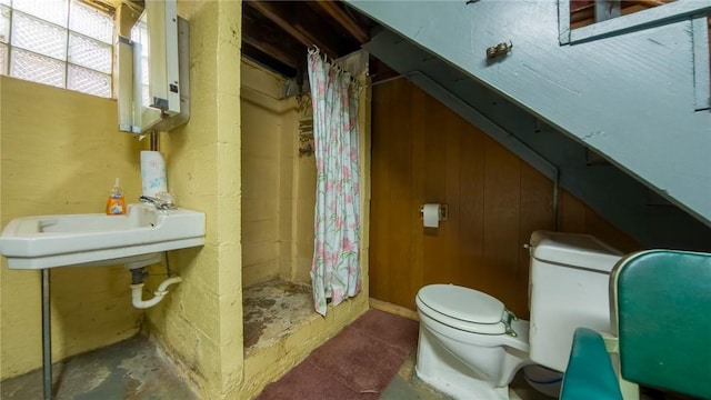 bathroom with toilet, wood walls, a shower with shower curtain, tankless water heater, and sink