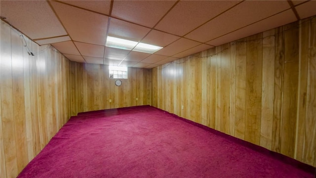 basement with a drop ceiling and wooden walls