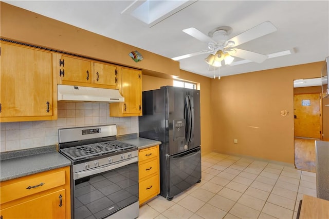 kitchen with black fridge, stainless steel range with gas cooktop, decorative backsplash, and a skylight