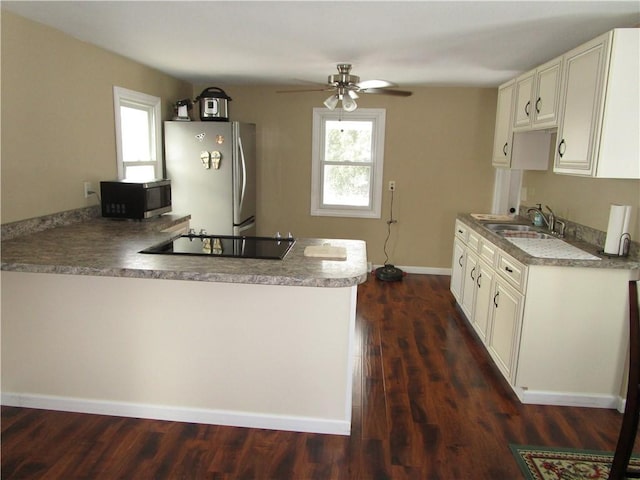 kitchen featuring kitchen peninsula, stainless steel fridge, black electric stovetop, ceiling fan, and sink