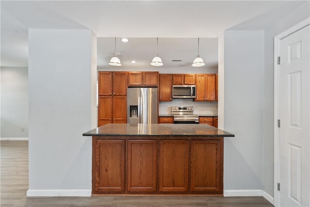 kitchen with appliances with stainless steel finishes, pendant lighting, dark stone counters, and wood-type flooring