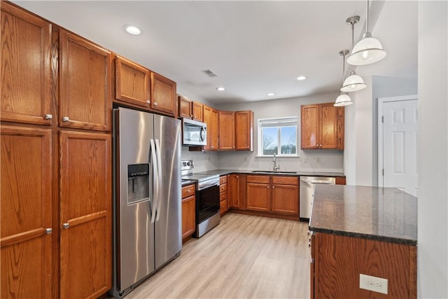 kitchen featuring stainless steel appliances, sink, dark stone countertops, light wood-type flooring, and hanging light fixtures