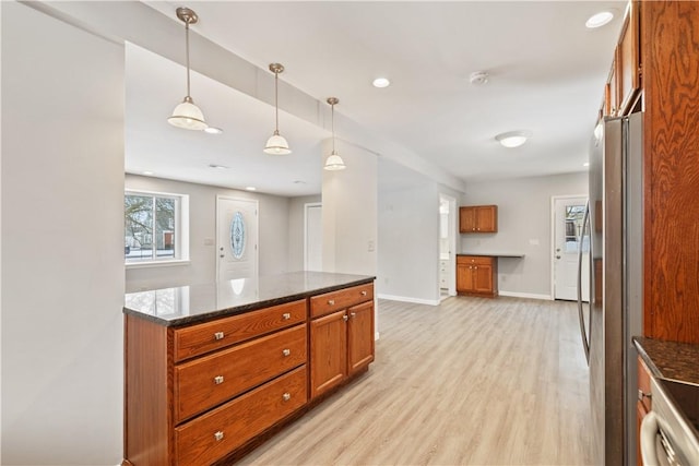 kitchen featuring decorative light fixtures, dark stone countertops, light hardwood / wood-style floors, and stainless steel fridge