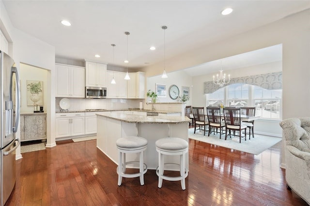 kitchen featuring stainless steel appliances, white cabinetry, decorative light fixtures, and a center island