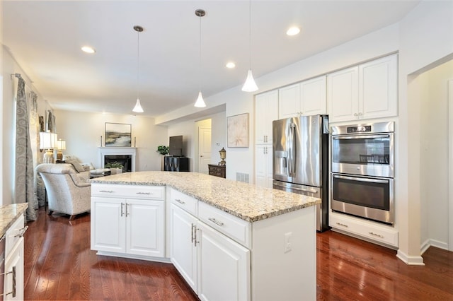 kitchen with light stone counters, decorative light fixtures, a kitchen island, white cabinets, and appliances with stainless steel finishes