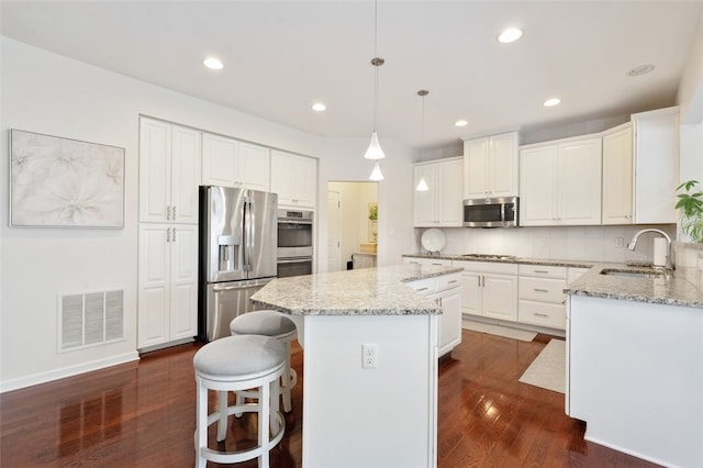 kitchen with a center island, decorative light fixtures, white cabinets, appliances with stainless steel finishes, and sink