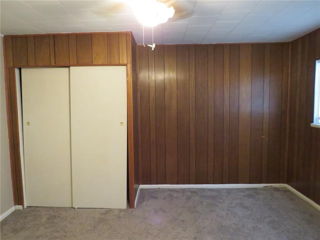 unfurnished bedroom with wooden walls, a closet, and light carpet