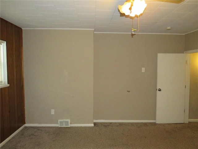 empty room with ornamental molding, wooden walls, and carpet