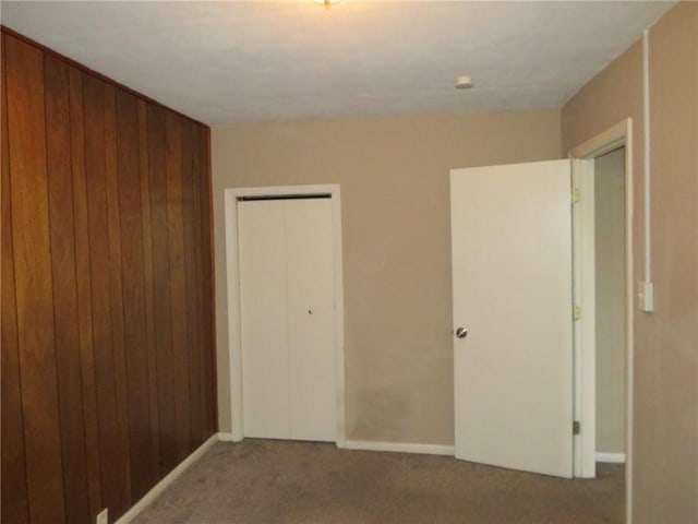 unfurnished bedroom featuring a closet, wood walls, and carpet