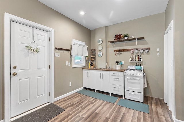 interior space featuring hardwood / wood-style floors, white cabinets, white gas range oven, and sink