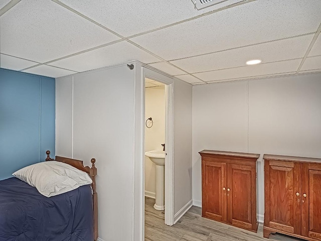 bedroom featuring sink, ensuite bath, a drop ceiling, and light hardwood / wood-style floors