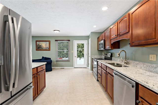 kitchen with stainless steel appliances, light tile patterned floors, a textured ceiling, light stone counters, and sink