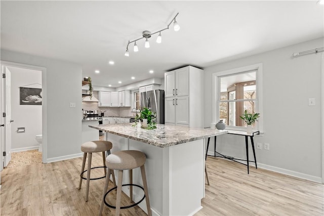 kitchen with stainless steel appliances, light wood-type flooring, light stone countertops, a breakfast bar, and white cabinetry