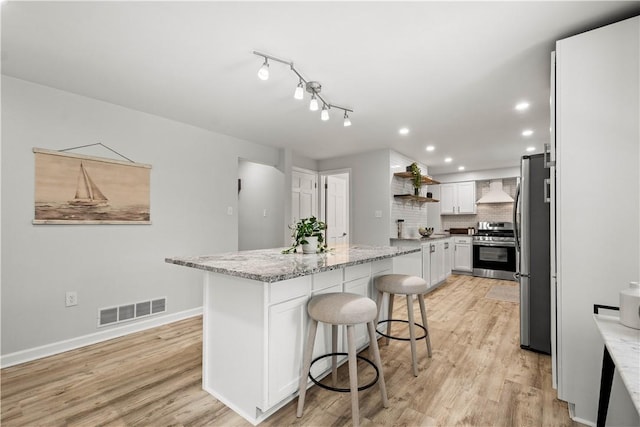 kitchen featuring stainless steel appliances, white cabinets, light stone counters, decorative backsplash, and a kitchen island