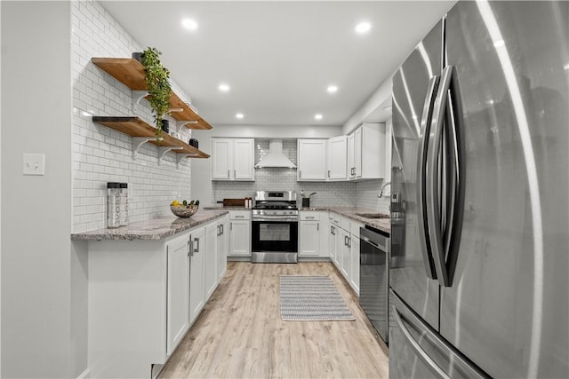 kitchen with stainless steel appliances, decorative backsplash, white cabinets, light hardwood / wood-style flooring, and wall chimney range hood