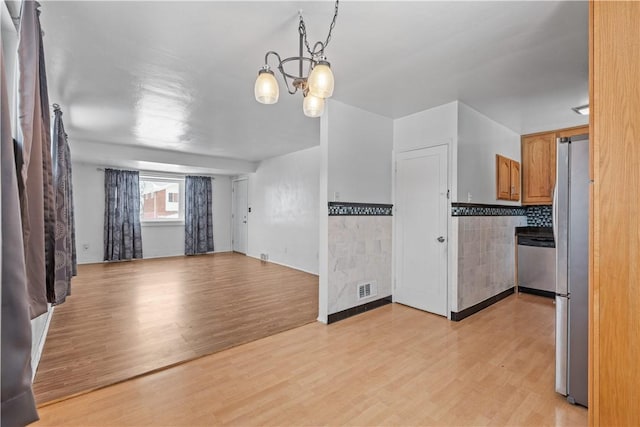 interior space featuring decorative light fixtures, stainless steel appliances, light hardwood / wood-style floors, decorative backsplash, and an inviting chandelier