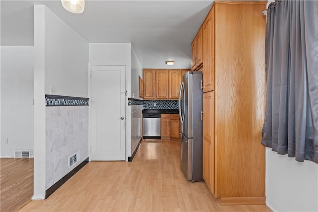 kitchen with appliances with stainless steel finishes, light hardwood / wood-style floors, and backsplash