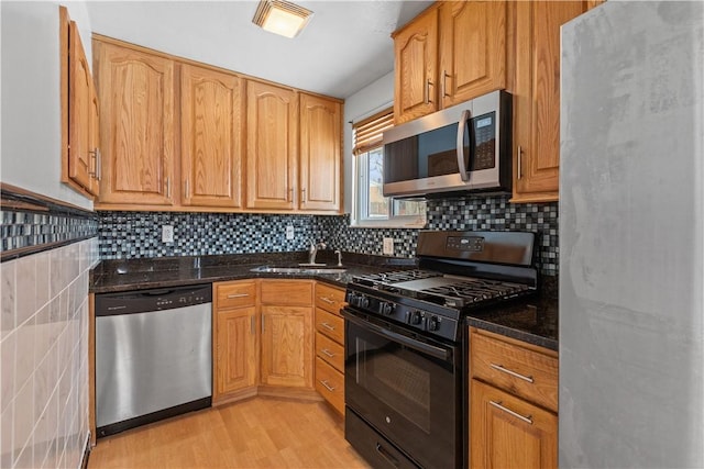 kitchen featuring appliances with stainless steel finishes, dark stone counters, sink, light hardwood / wood-style flooring, and tasteful backsplash