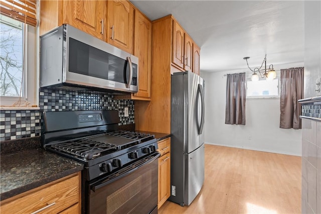 kitchen featuring dark stone countertops, appliances with stainless steel finishes, a notable chandelier, decorative backsplash, and light hardwood / wood-style flooring