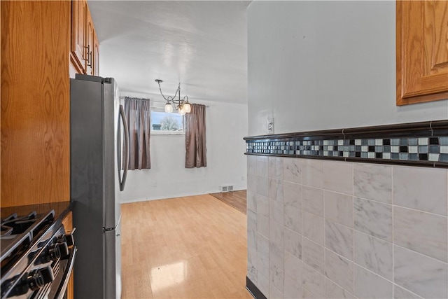 kitchen featuring stainless steel refrigerator, hanging light fixtures, gas stove, a notable chandelier, and light hardwood / wood-style flooring