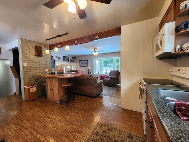 kitchen with sink, decorative light fixtures, white appliances, a kitchen bar, and dark hardwood / wood-style floors