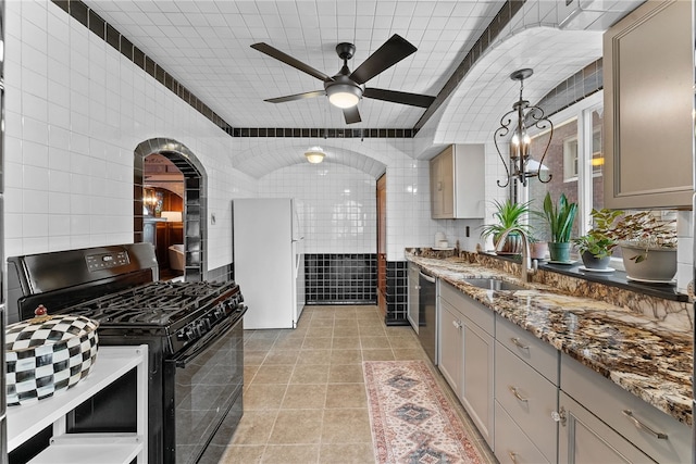 kitchen with dishwasher, dark stone countertops, black gas range oven, tile walls, and sink