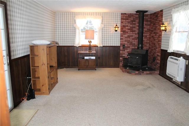 living room featuring light carpet, wooden walls, heating unit, and a wood stove