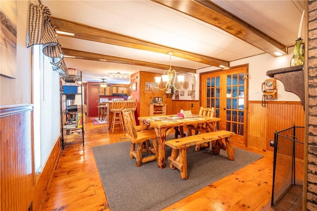 dining room with light hardwood / wood-style floors, french doors, wooden walls, and beamed ceiling