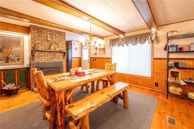 dining area featuring a fireplace, beamed ceiling, light hardwood / wood-style flooring, wood walls, and a chandelier