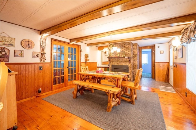 dining space with light hardwood / wood-style flooring, a brick fireplace, wooden walls, and beamed ceiling