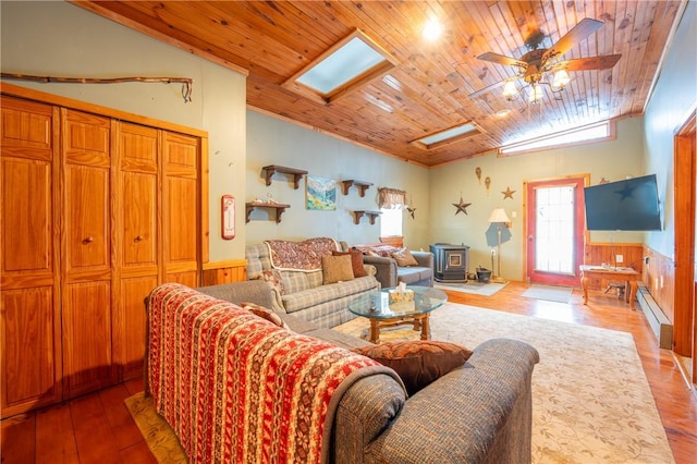 living room featuring a wood stove, ceiling fan, hardwood / wood-style floors, baseboard heating, and wood ceiling