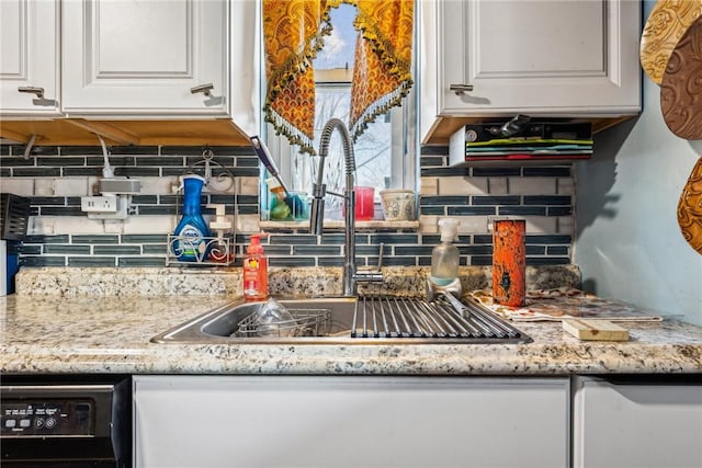 kitchen with light stone countertops, sink, black dishwasher, white cabinetry, and backsplash