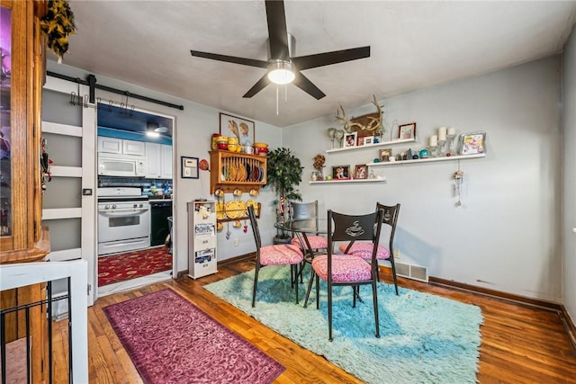 dining room featuring ceiling fan, wood-type flooring, and a barn door