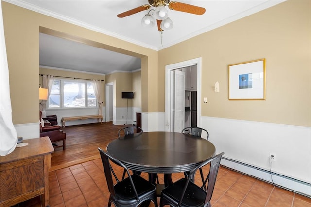 tiled dining space featuring ceiling fan, crown molding, and a baseboard heating unit