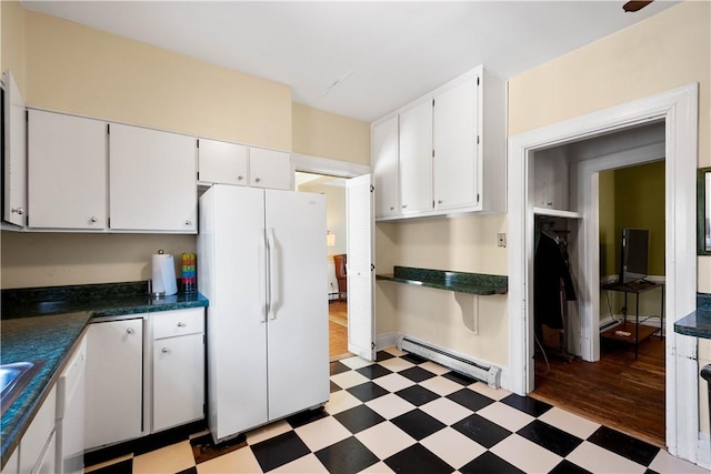 kitchen with baseboard heating, white fridge, and white cabinetry