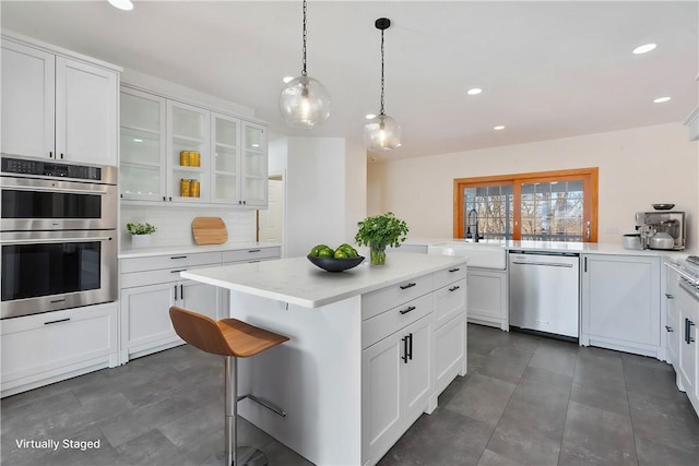 kitchen with decorative light fixtures, a kitchen island, sink, stainless steel appliances, and white cabinets