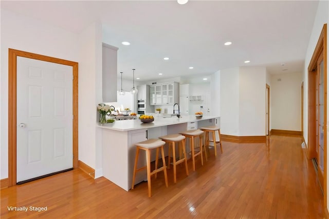 kitchen featuring light hardwood / wood-style floors, kitchen peninsula, hanging light fixtures, a breakfast bar area, and white cabinets