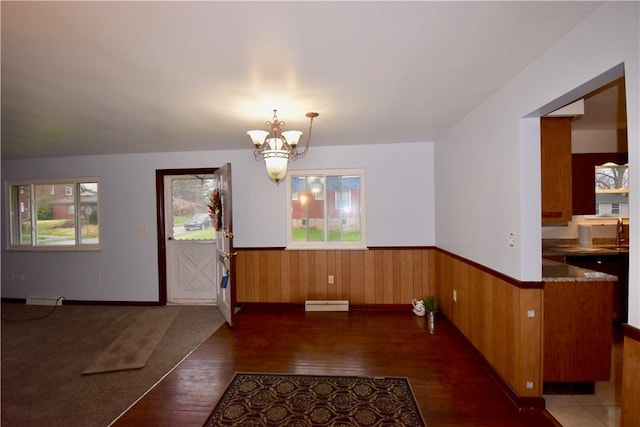 unfurnished dining area featuring sink, dark hardwood / wood-style flooring, baseboard heating, and a notable chandelier