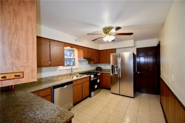 kitchen featuring stainless steel appliances, sink, dark stone countertops, ceiling fan, and wood walls