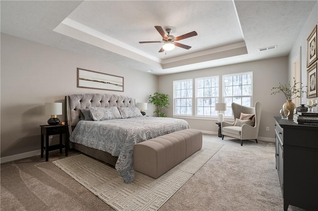 bedroom featuring light carpet, ceiling fan, and a tray ceiling