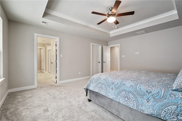 bedroom with ceiling fan, light colored carpet, and a tray ceiling