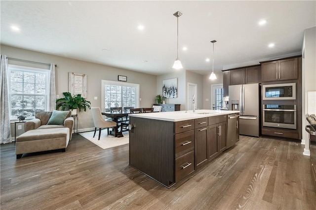 kitchen with stainless steel appliances, an island with sink, hanging light fixtures, dark hardwood / wood-style floors, and dark brown cabinets