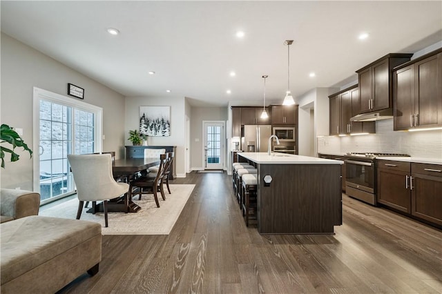 kitchen with dark brown cabinets, pendant lighting, an island with sink, and appliances with stainless steel finishes